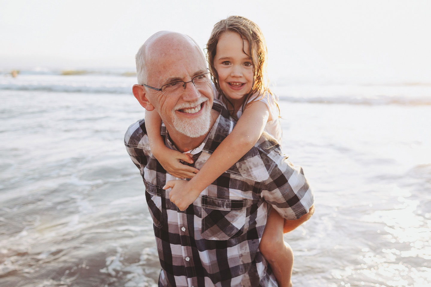 Fokussiert auf den Mensch: Grossvater hält seine Enkelin im Huckepack am Meer