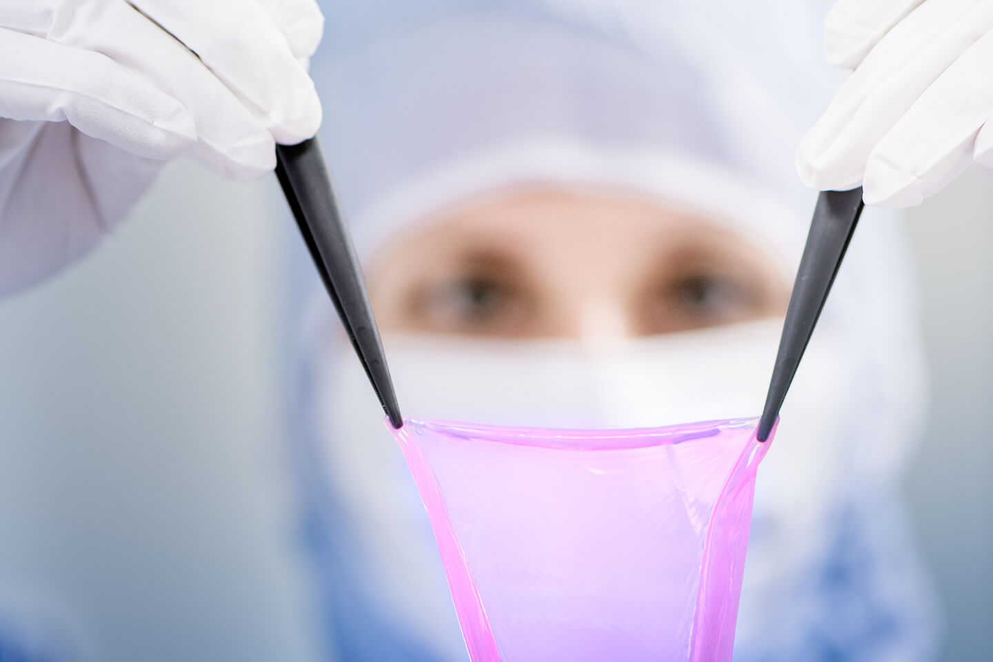 Laborsituation einer Forscherin, die mit Pinzetten-Instrumenten ein textilartiges Gewebe hochhebt.