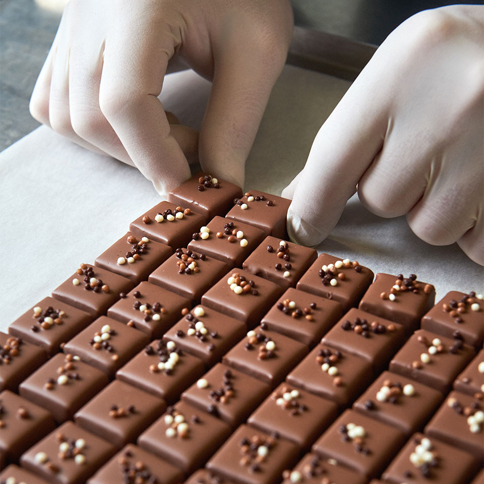 Emotionale und clevere Website: Hände reihen Pralines an Pralines an.